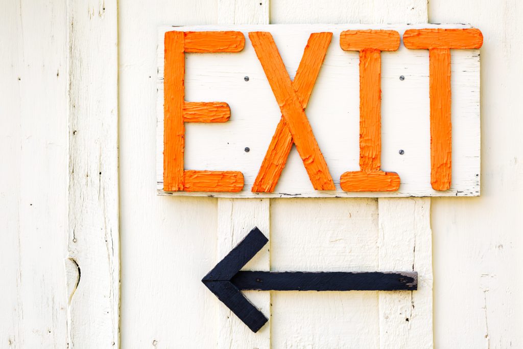 Exit strategy sign in orange letters on white fence