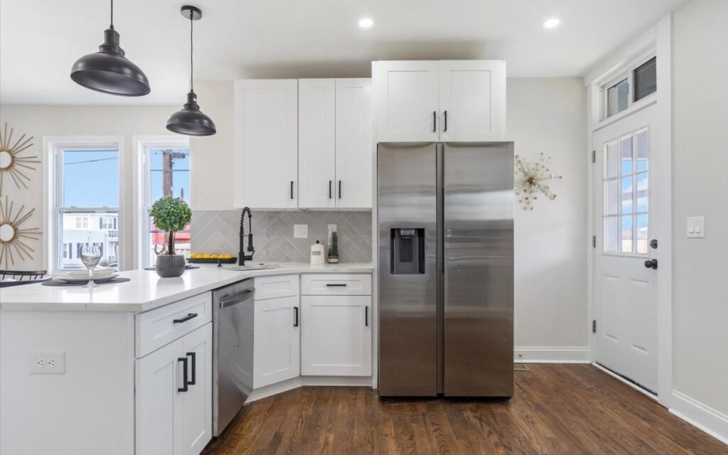The picture of white kithchen with a stainless steel refrigerator.